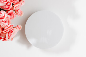 Empty white round podium with pink flowers and sunlight shadows on white wooden background,...
