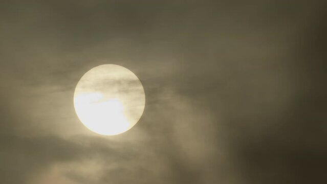 A veiled sun partially obscured by clouds, creating a muted glow against a dark sky