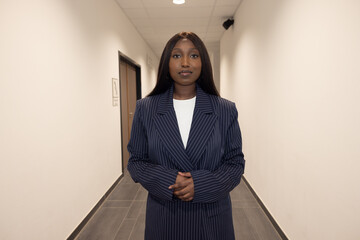 This photograph captures a poised young adult Black woman standing confidently in an office...