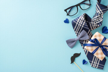 Show appreciation for Dad on Father's Day with tasteful top view arrangement comprising elegant necktie, bow tie, giftbox, glasses, mustache on tranquil blue background, perfect for your promotions