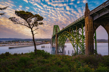 Sunset over Yaquina Bay Bridge in Newport, Oregon with cloudy sky. The Yaquina Bay Bridge is an elegant art deco structure arching over the picturesque bay.