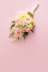Brush paints with flowers, spring concept on pastel pink background. Minimal nature flat lay. A copy space. Vertical view.