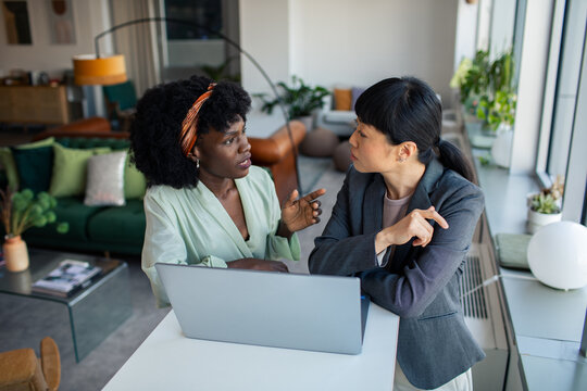 Two young businesswomen discussing work over laptop in office