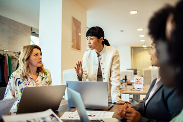 Diverse female business team working and smiling at office desk with laptop