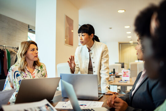 Diverse female business team working and smiling at office desk with laptop