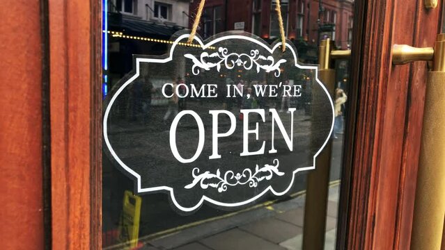 A restaurant door entrance sign reading come in, we're open. Concept for business, food, drink and hospitality. Eating out in the West End of London. Static shot 4K.
