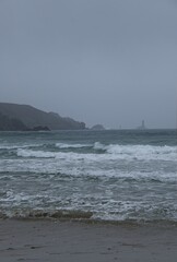 Wonderful landscapes in France, Brittany. Baie des Trepasses Beach in Plogoff. Surfers and Old Lighthouse (Phare de la Vieille). Cloudy spring day. Selective focus.