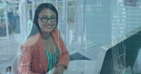 About a young businesswoman of biracial who is working on a computer and smiling at the camera