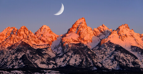 Sunrise on Teton Mountain Range in Wyoming Alpen Glow Orange and Pink on Rugged Mountains with Crescent Moon