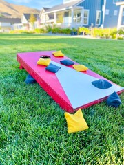 Red and white cornhole board with bean bags on lawn in summer, leisure game activity