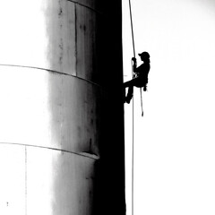Silhouette of Person on Ropes Painting Sign on Side of Building Silo