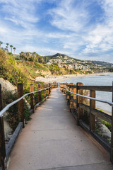A wooden boardwalk leads to the beach. The boardwalk is lined with trees and has a railing. The beach is a beautiful, serene place with the ocean in the background