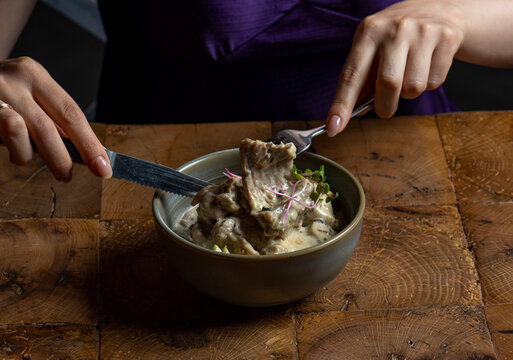 Woman eating rack of lamb in cream sauce with apple and radish in a bowl
