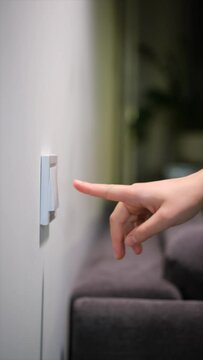 A woman's hand turns on and off the light by pressing the switch button in the room. Lights on and off.