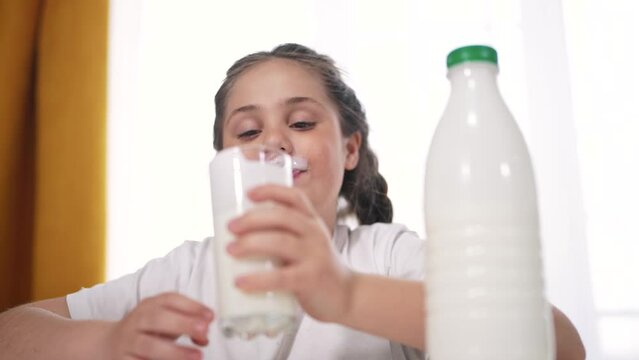 child dirty drinks milk. healthy a eating children concept. child girl drinks milk in lifestyle the kitchen stained lips funny rejoices smiling. daughter whale drinks milk