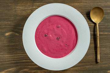 Sweet summer cherry soup in a white plate on a wooden background, closeup, top view. Hungarian cold red cherry soup with yogurt or cream