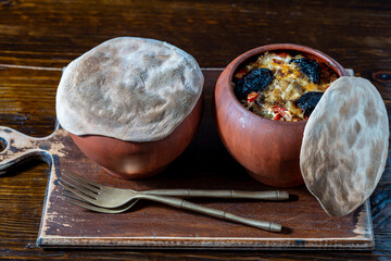 Two clay pots with stewed vegetables on a wooden table, closeup. Stewing food in earthenware is considered healthy - 785509534