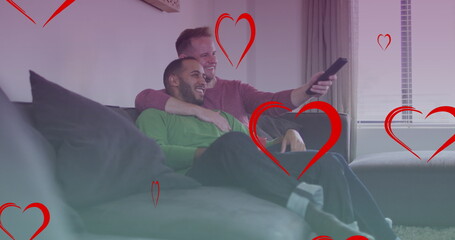 Image of heart icons over diverse gay couple smiling and watching tv