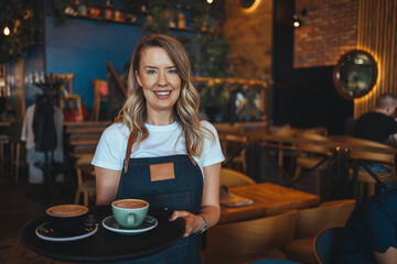 Cheerful young waitress wearing apron laughing looking at camera, happy businesswoman small business owner of girl entrepreneur cafe employee posing in restaurant coffee shop interior, portrait