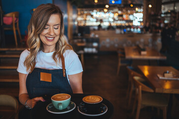 Portrait of a beautiful waitress wearing an apron, smiling at camera. Female barista in her 20s...