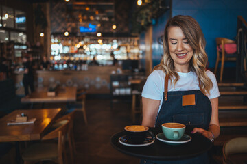 Portrait of girl, student working part-time in cafe, holding cup of coffee, made order, looking for...