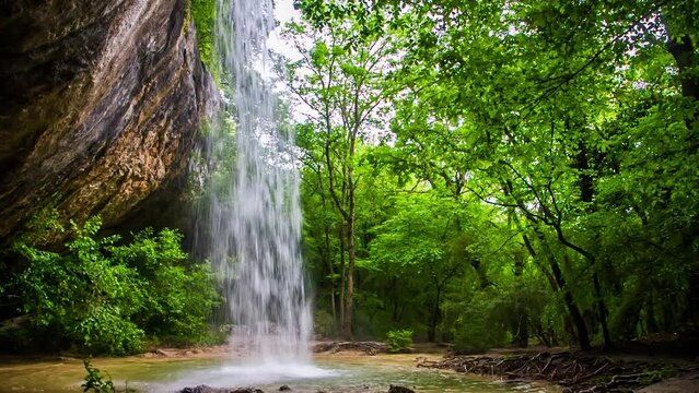 a waterfall from a rock forms a cave in a deep forest HD 