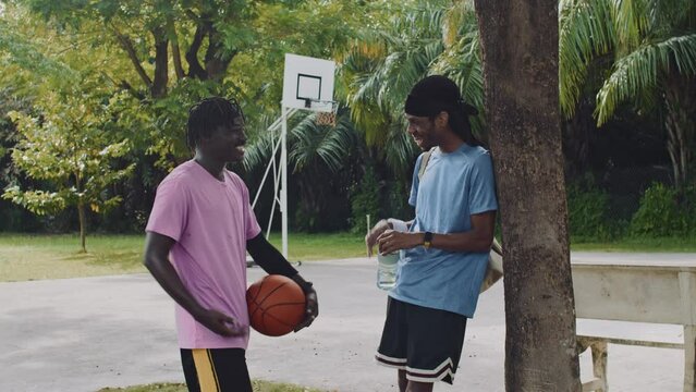 Medium long shot of two African American guys chatting after game on basketball court outdoors