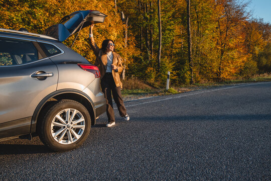 a smiling man with a backpack on his back closes the trunk of the car in autumn season. copy space