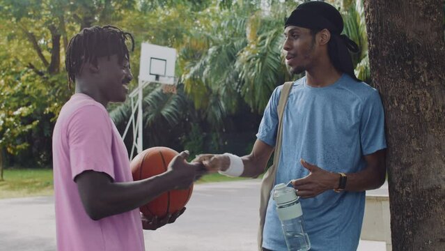 Medium shot of two black sportsmen saying goodbye after streetball training on outdoor court
