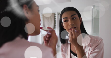 Image of light spots over biracial woman applying lipstick