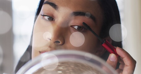 Image of light spots over biracial woman applying mascara - Powered by Adobe
