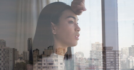 Fototapeta premium Image of cityscape over biracial woman looking through window