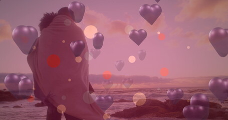 Image of purple hearts over couple in love by seaside - obrazy, fototapety, plakaty