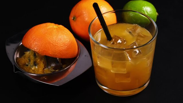 Spremuta di arancia nel bicchiere con cannuccia e ghiaccio, spremiagrumi con buccia di arancia sul tavolo