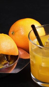 bicchiere con spremuta d'arancia e ghiaccio, cannuccia nera, spremiagrumi con buccia di arancia, video verticale