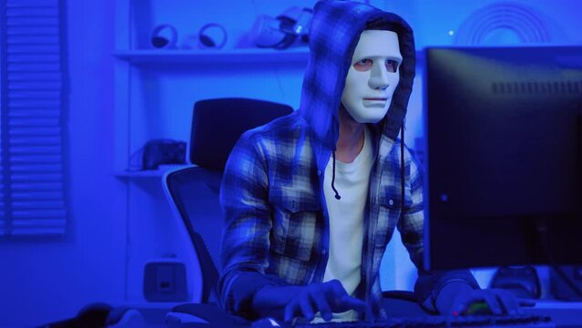 hacker wearing a white mask is using a computer to steal confidential information.Concepts: computer crime, burglary, business security on computer networks
