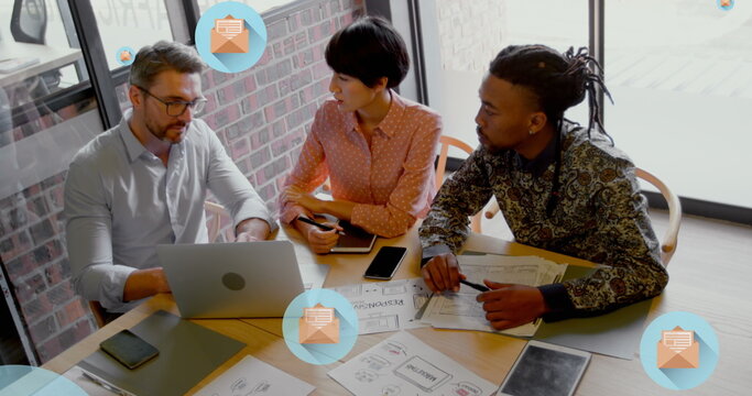 Image of letter in open envelope icons over diverse coworkers discussing on desk in office