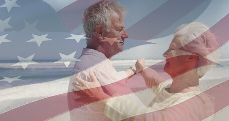 Image of happy senior caucasian couple dancing on beach over flag of united states of america