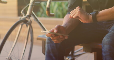 Image of biracial man sitting and using smartphone with bicycle - Powered by Adobe