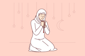 Muslim woman honors holy month of ramadan, reading prayer sitting on knees, wearing islamic or arabic traditional clothing. Praying girl smiles, celebrating onset of ramadan and thanks allah - 785544150