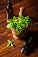 Fresh mint leafs in vintage mortar, essential oil on wooden table