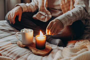a caucasian man relaxing at home, lighting candle, drinking coffee in bed
