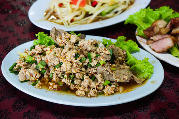 Spicy minced pork salad on dish with other Thai food on table