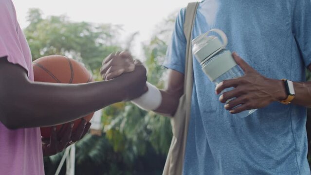 Cropped shot of two male streetball players shaking hands while thanking each other for good game on outdoor court