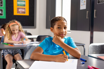 In school, young biracial male student sitting at a desk in a classroom, looking thoughtful - Powered by Adobe