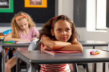 In school, young biracial female student sitting at a desk in a classroom, looking thoughtful