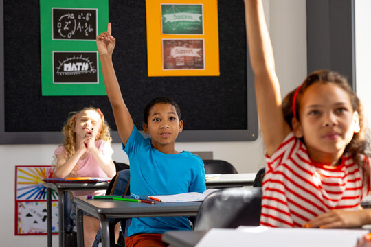 In school, diverse group of young students sitting at desks in a classroom, raising hands