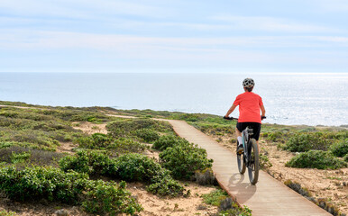 nice senior woman riding her electric mountain bike at the rocky and sandy coastline of the...