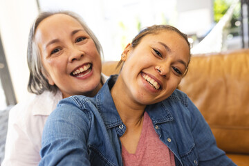 Asian grandmother and biracial teenage granddaughter are smiling together at home - 785549769