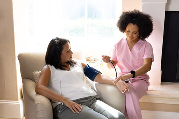Mature biracial woman getting blood pressure checked by young biracial nurse at home - Powered by Adobe